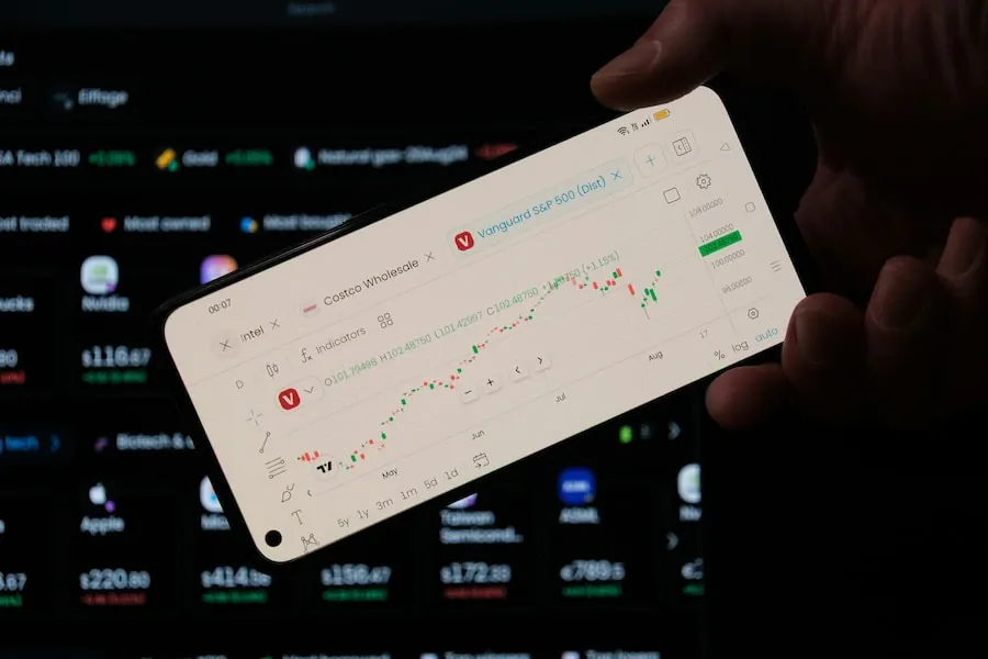 A person checking market data on a phone beside a laptop
