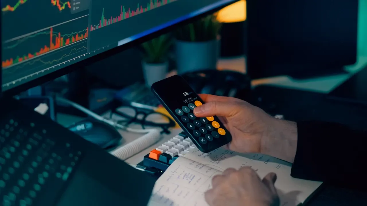 Trader analyzing drawdown and risk metrics on computer charts with a calculator