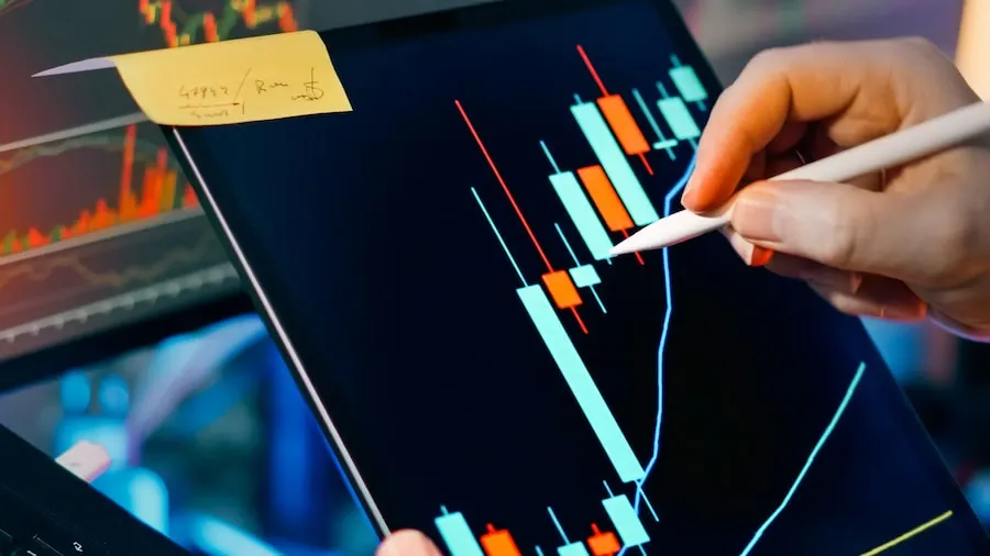 A trader analysing market charts on a tablet and monitor