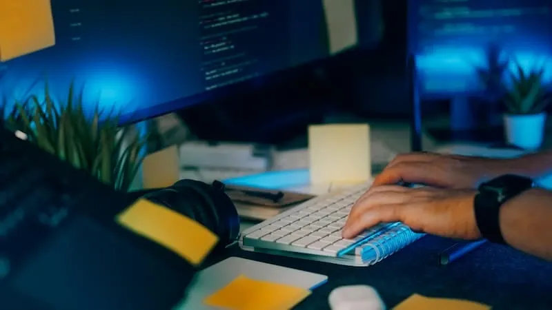 Hands typing on a keyboard beside code screens