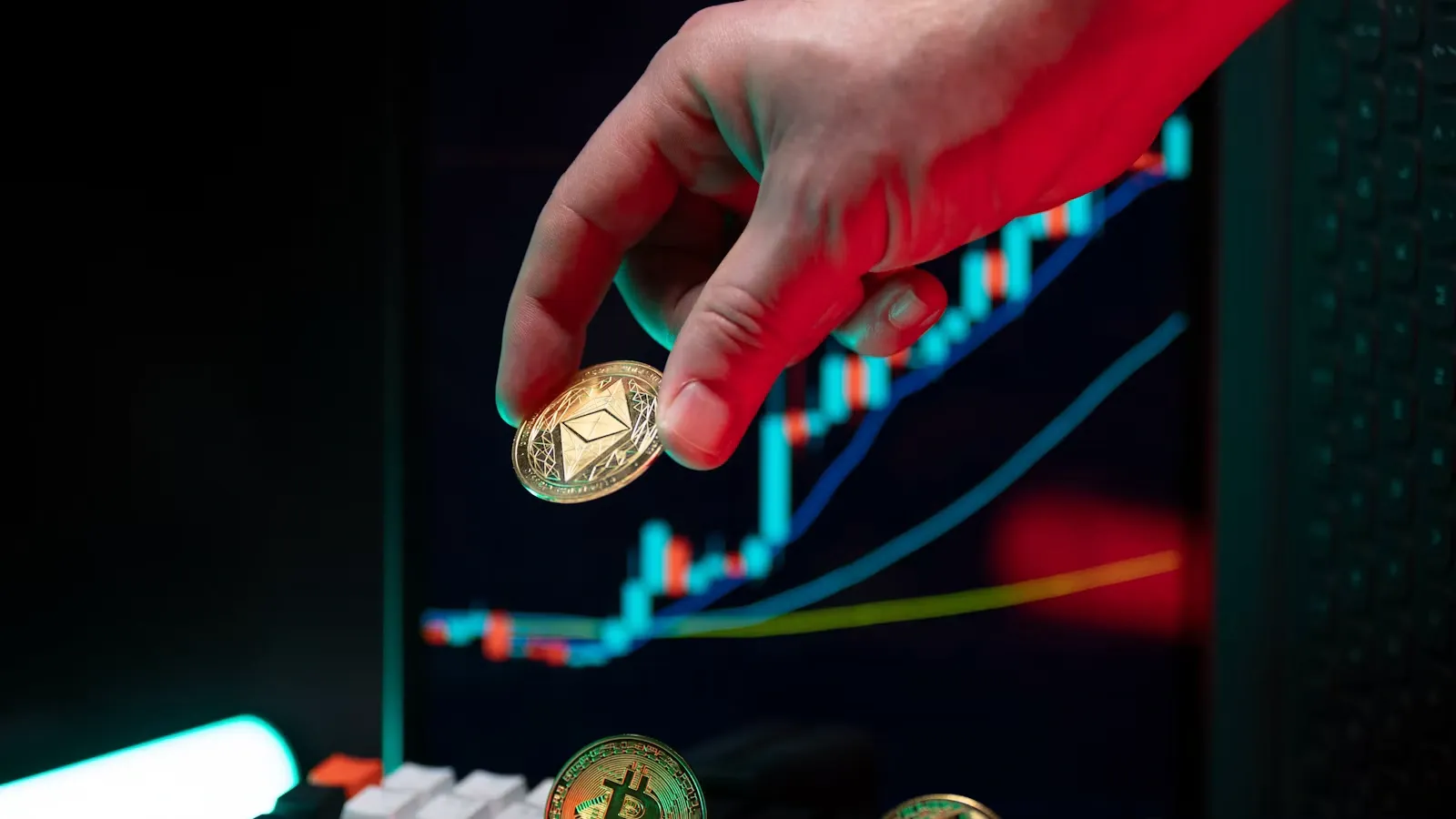 A hand holding a coin before market graphs