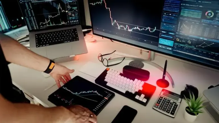 A person analyzing market charts at a desk with two monitors and a laptop
