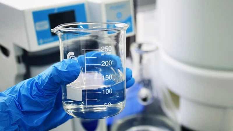 A gloved hand holding a beaker